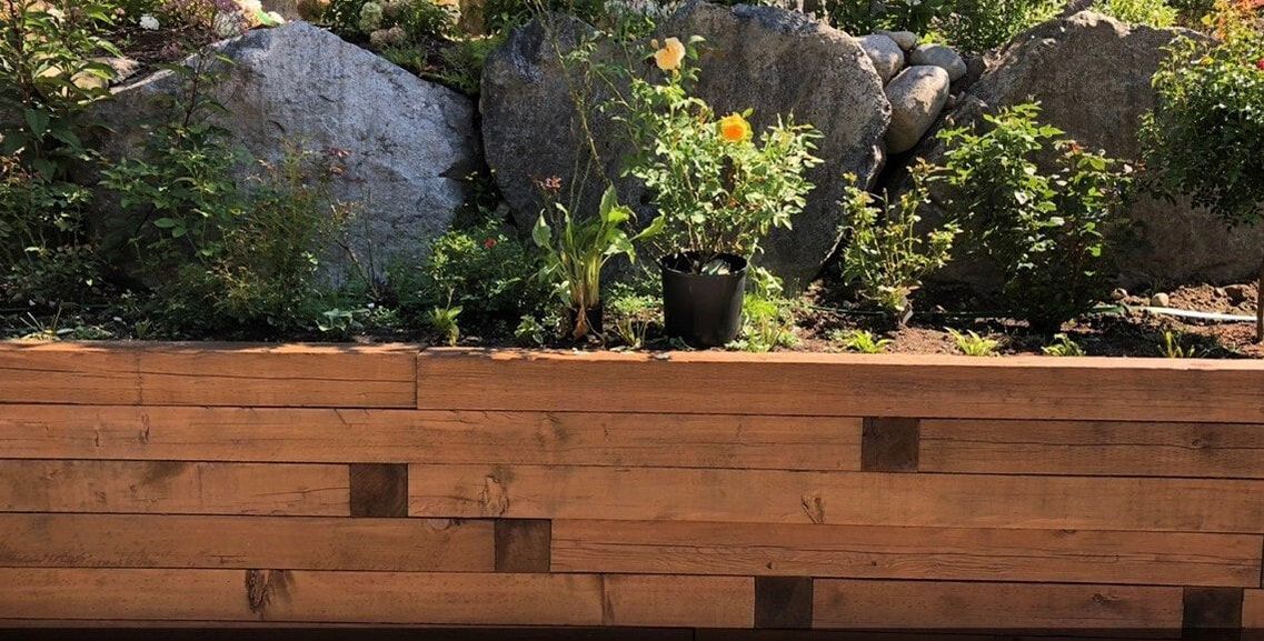 wooden retaining wall with plants and boulders